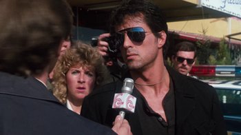 Movie still from “Cobra” (1986), directed by George P. Cosmatos – A man is being interviewed by a reporter; Close Up shot, Over the shoulder angle