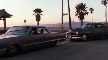 Movie still from “Cobra” (1986), directed by George P. Cosmatos – A couple of cars driving down a street next to palm trees; Wide shot, Low angle