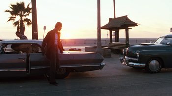 Movie still from “Cobra” (1986), directed by George P. Cosmatos – A man standing next to a car on the street; Wide shot, Low angle