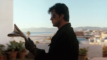 Movie still from “Cobra” (1986), directed by George P. Cosmatos – A man in a black jacket is looking at a paper; Medium shot, Low angle