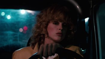 Movie still from “Cobra” (1986), directed by George P. Cosmatos – A woman sitting in the drivers seat of a car at night; Close Up shot, Low angle