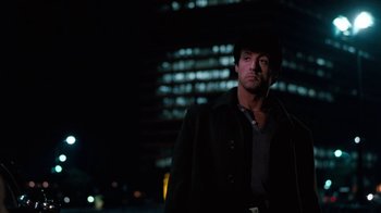 Movie still from “Cobra” (1986), directed by George P. Cosmatos – A man standing in front of a tall building at night; Medium shot, Low angle