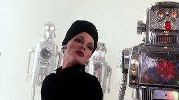 Movie still from “Cobra” (1986), directed by George P. Cosmatos – A woman in a black hat standing in front of a wall of robots; Close Up shot, Low angle