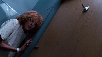 Movie still from “Cobra” (1986), directed by George P. Cosmatos – A woman with red hair is peeking out from behind a door; Medium shot, Low angle