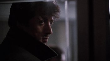 Movie still from “Cobra” (1986), directed by George P. Cosmatos – A person looking out of a window; Close Up shot, Over the shoulder angle