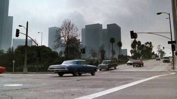 Movie still from “Cobra” (1986), directed by George P. Cosmatos – Cars driving down a street in front of tall buildings; Extreme Wide shot, Low angle