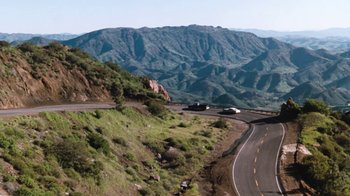 Movie still from “Cobra” (1986), directed by George P. Cosmatos – A road going down a hill with a mountain in the background; Extreme Wide shot, High angle
