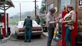 Movie still from “Cobra” (1986), directed by George P. Cosmatos – A couple of people that are at a gas pump; Wide shot, Over the shoulder angle