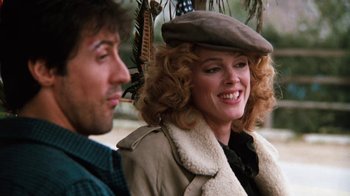 Movie still from “Cobra” (1986), directed by George P. Cosmatos – A man and a woman sitting next to each other; Close Up shot, Over the shoulder angle