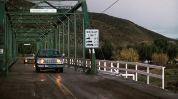 Movie still from “Cobra” (1986), directed by George P. Cosmatos – A car driving down a bridge with a sign on it; Extreme Wide shot, High angle