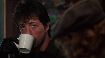 Movie still from “Cobra” (1986), directed by George P. Cosmatos – A person drinking a cup of coffee; Close Up shot, Over the shoulder angle