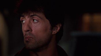 Movie still from “Cobra” (1986), directed by George P. Cosmatos – A man with a black shirt is looking at the camera; Close Up shot, Low angle