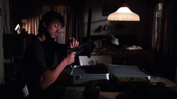 Movie still from “Cobra” (1986), directed by George P. Cosmatos – A man holding a gun while standing in a room; Medium shot, Low angle