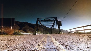 Movie still from “Cobra” (1986), directed by George P. Cosmatos – An empty road in the middle of a desert area; Extreme Wide shot, Low angle