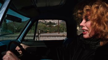 Movie still from “Cobra” (1986), directed by George P. Cosmatos – A woman sitting in the driver's seat of a car; Close Up shot, Low angle