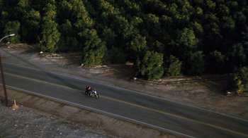 Movie still from “Cobra” (1986), directed by George P. Cosmatos – Two people riding a motorcycle down the side of a road; Extreme Wide shot, High angle