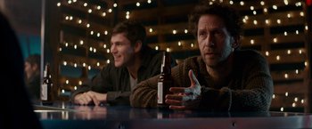 Movie still from “Colossal” (2016), directed by Nacho Vigalondo – Two men sitting at a table with a bottle of beer; Medium shot, Over the shoulder angle