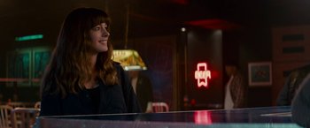 Movie still from “Colossal” (2016), directed by Nacho Vigalondo – A woman sitting at a table in front of a neon sign; Medium shot, Over the shoulder angle