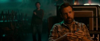 Movie still from “Colossal” (2016), directed by Nacho Vigalondo – A man sitting in front of another man in a dark room; Close Up shot, Over the shoulder angle