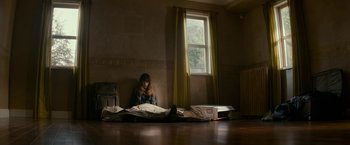 Movie still from “Colossal” (2016), directed by Nacho Vigalondo – A woman sitting on the floor in front of an open window; Wide shot, High angle