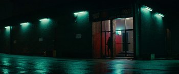 Movie still from “Colossal” (2016), directed by Nacho Vigalondo – A person standing in front of a building at night; Extreme Wide shot, Low angle