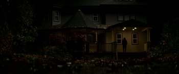 Movie still from “Colossal” (2016), directed by Nacho Vigalondo – A person standing in front of a house at night; Extreme Wide shot, High angle