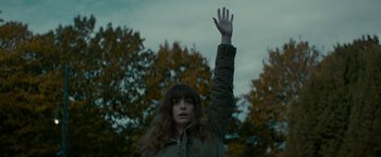 Movie still from “Colossal” (2016), directed by Nacho Vigalondo – A woman with long brown hair raising her hand in front of trees; Medium shot, Low angle