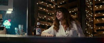 Movie still from “Colossal” (2016), directed by Nacho Vigalondo – A woman sitting in front of a bottle of beer; Medium shot, Over the shoulder angle