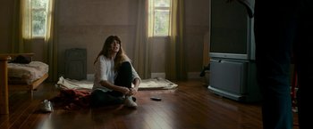 Movie still from “Colossal” (2016), directed by Nacho Vigalondo – A woman sitting on the ground in a room; Wide shot, High angle