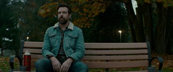 Movie still from “Colossal” (2016), directed by Nacho Vigalondo – A man sitting on top of a wooden park bench; Medium shot, Over the shoulder angle