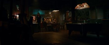 Movie still from “Colossal” (2016), directed by Nacho Vigalondo – A group of people sitting around a table in a room; Wide shot, High angle