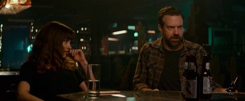 Movie still from “Colossal” (2016), directed by Nacho Vigalondo – A man sitting at a table in front of a glass of water; Medium shot, Over the shoulder angle