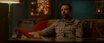 Movie still from “Colossal” (2016), directed by Nacho Vigalondo – A man sitting at a table in front of a painting on the wall; Medium shot, Over the shoulder angle