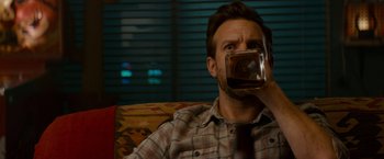 Movie still from “Colossal” (2016), directed by Nacho Vigalondo – A man sitting on a couch drinking a glass of beer; Close Up shot, Over the shoulder angle