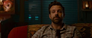 Movie still from “Colossal” (2016), directed by Nacho Vigalondo – A person sitting on a couch wearing a tie; Close Up shot, Over the shoulder angle