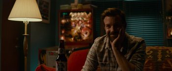 Movie still from “Colossal” (2016), directed by Nacho Vigalondo – A man sitting in front of a television with a beer; Close Up shot, Over the shoulder angle