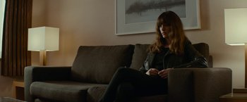 Movie still from “Colossal” (2016), directed by Nacho Vigalondo – A woman sitting on top of a brown couch; Medium shot, Over the shoulder angle