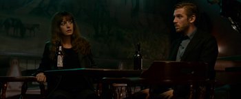 Movie still from “Colossal” (2016), directed by Nacho Vigalondo – A woman sitting at a table with a bottle of wine; Medium shot, Over the shoulder angle
