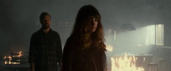 Movie still from “Colossal” (2016), directed by Nacho Vigalondo – A woman standing next to a man in a dark room; Medium shot, Over the shoulder angle