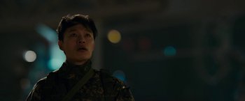 Movie still from “Colossal” (2016), directed by Nacho Vigalondo – A man in a military uniform standing next to lights; Close Up shot, Low angle