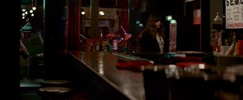 Movie still from “Colossal” (2016), directed by Nacho Vigalondo – A woman sitting at a bar in a dark room; Wide shot, Over the shoulder angle