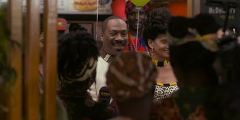 Movie still from “Coming 2 America” (2021), directed by Craig Brewer – A group of people standing next to each other in a room; Medium shot, Over the shoulder angle
