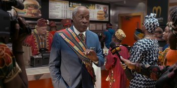 Movie still from “Coming 2 America” (2021), directed by Craig Brewer – An older man in a suit and a colorful neck tie; Medium shot, Over the shoulder angle