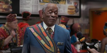 Movie still from “Coming 2 America” (2021), directed by Craig Brewer – An older man in a blue suit with a colorful tie; Close Up shot, Over the shoulder angle