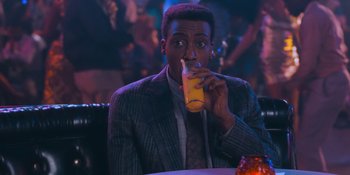 Movie still from “Coming 2 America” (2021), directed by Craig Brewer – A man sitting at a table with a drink in front of him; Close Up shot, High angle