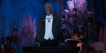 Movie still from “Coming 2 America” (2021), directed by Craig Brewer – An older man in a tuxedo standing in front of a table; Medium shot, Low angle