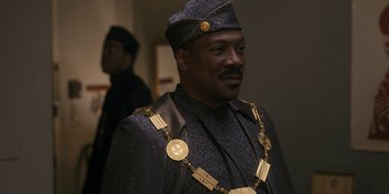Movie still from “Coming 2 America” (2021), directed by Craig Brewer – A man in a black suit and a gold chain around his neck; Close Up shot, Over the shoulder angle