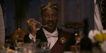 Movie still from “Coming 2 America” (2021), directed by Craig Brewer – A man in a suit and a crown is holding a spoon in his mouth; Close Up shot, Low angle