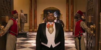 Movie still from “Coming 2 America” (2021), directed by Craig Brewer – A man in a black suit and a gold medal; Medium shot, Over the shoulder angle