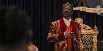 Movie still from “Coming 2 America” (2021), directed by Craig Brewer – A man wearing a suit and a crown standing in front of a curtain; Medium shot, Over the shoulder angle